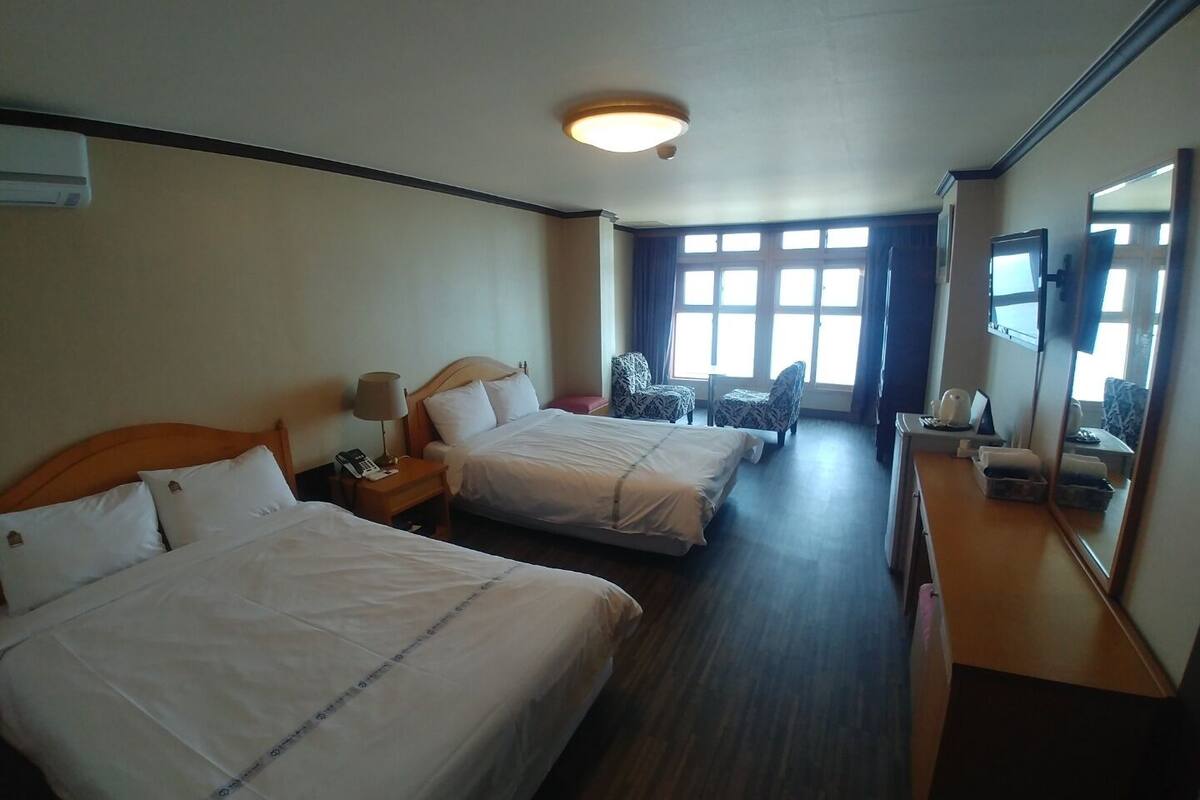 A hotel room with two beds, a desk, a chair, a mirror, and a window with curtains.