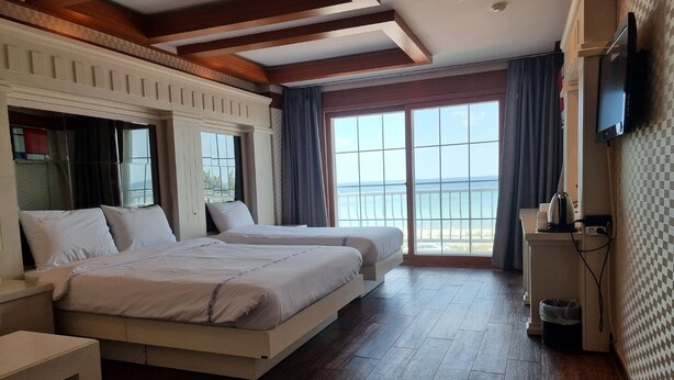 Ein Hotelzimmer mit zwei Betten, einem Fernseher und einem Balkon mit Meerblick.