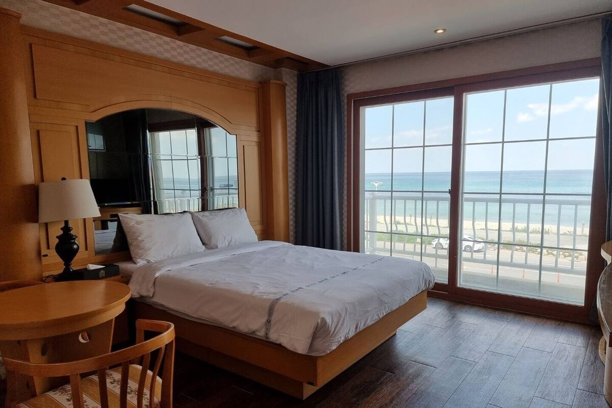 A hotel room with a large bed, a desk, a chair, and a view of the beach.