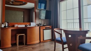 Ein Hotelzimmer mit Schreibtisch aus Holz, einem Sessel, einem kleinen Tisch, einem Fernseher und einem großen Fenster.