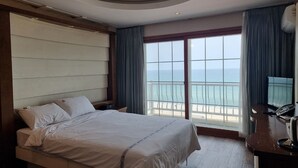 Ein Hotelzimmer mit einem großen Bett, einem Schreibtisch mit Telefon und Blick auf das Meer durch ein großes Fenster.