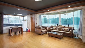 Un salon spacieux doté d’un plancher en bois, d’un ensemble de canapés, d’une table basse et d’une grande fenêtre donnant sur un paysage verdoyant.