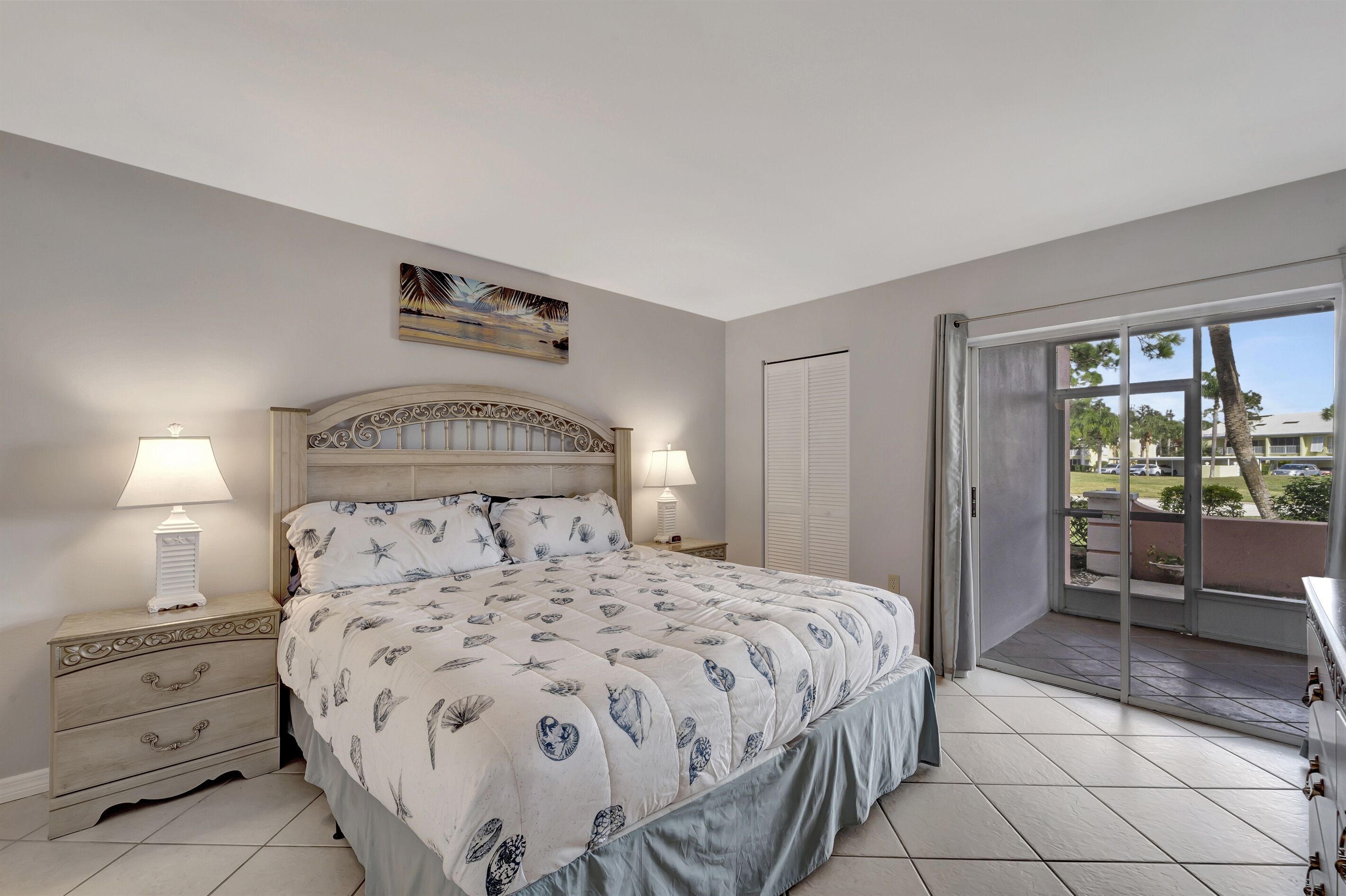 Een slaapkamer met een bed, twee bedlampen, een nachtkastje, een raam met uitzicht en een deur naar een buitenruimte.