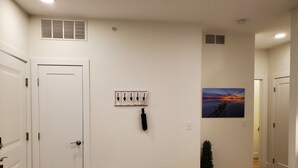 A hallway with a white door, a coat rack, a small plant, and a painting of a sunset. - Capri 107 Downtown Traverse City  (Traverse City)