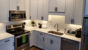 A modern kitchen with white cabinets, stainless steel appliances, and a tiled backsplash. - Capri 107 Downtown Traverse City  (Traverse City)