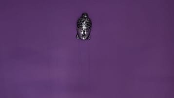 Una cama con cabecera morada, un Buda decorativo y arreglos florales que deletrean “HAPPY BIRTHDAY” sobre el edredón.