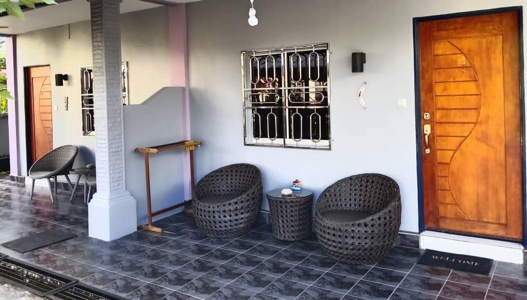 A covered porch with two wicker chairs, a small table, and a wooden door with a metal gate.