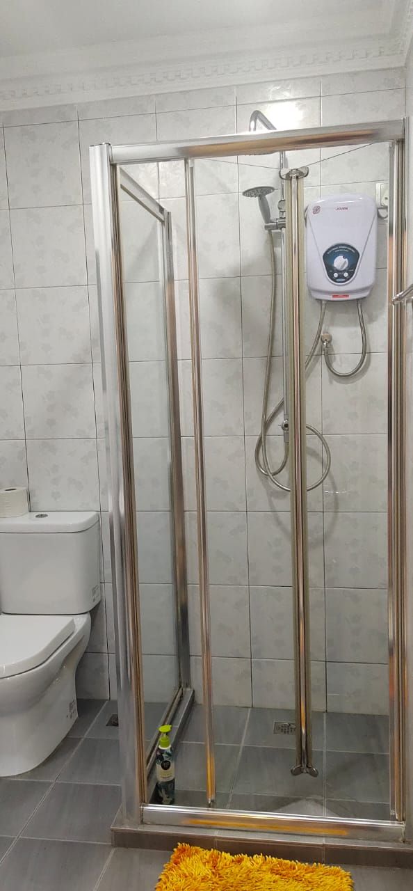 A glass-enclosed shower stall with a handheld showerhead and a wall-mounted control panel.