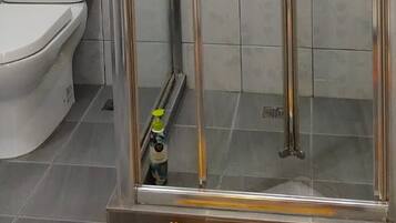 A glass-enclosed shower stall with a handheld showerhead and a wall-mounted control panel.