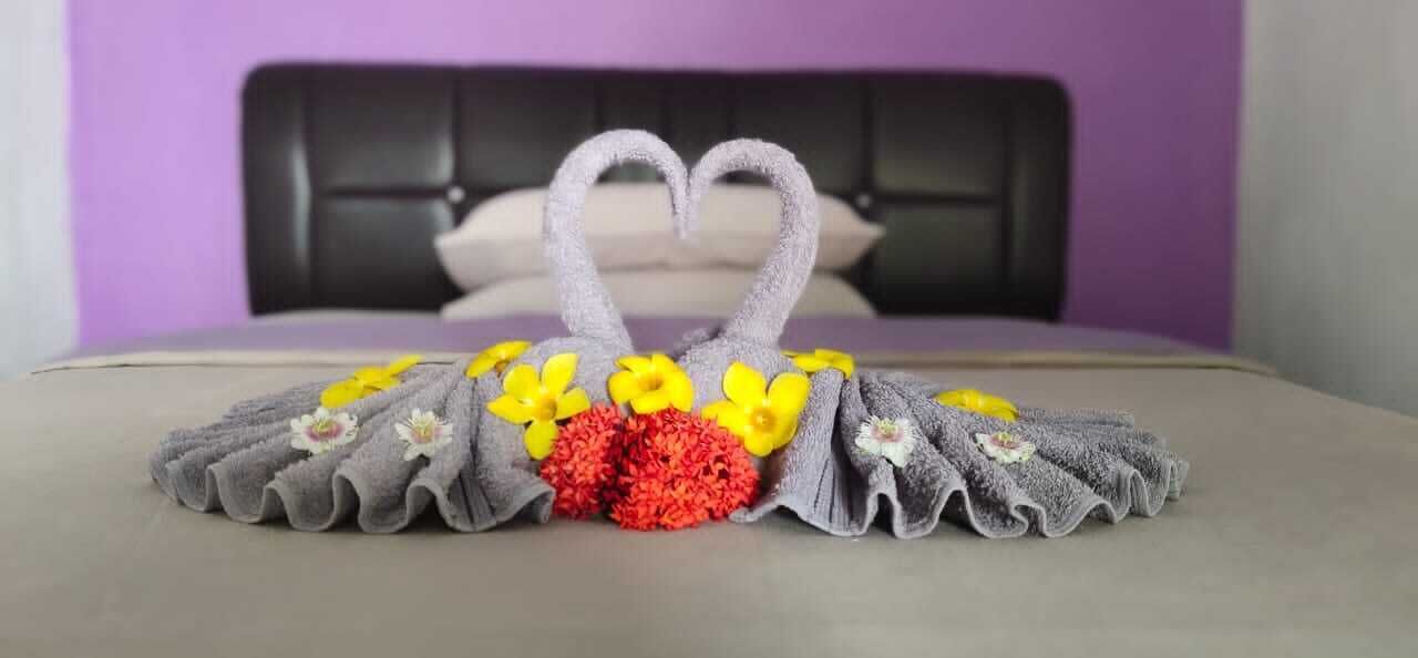 Een bed met een handdoek gerangschikt in de vorm van een hart en bloemen op een sprei.