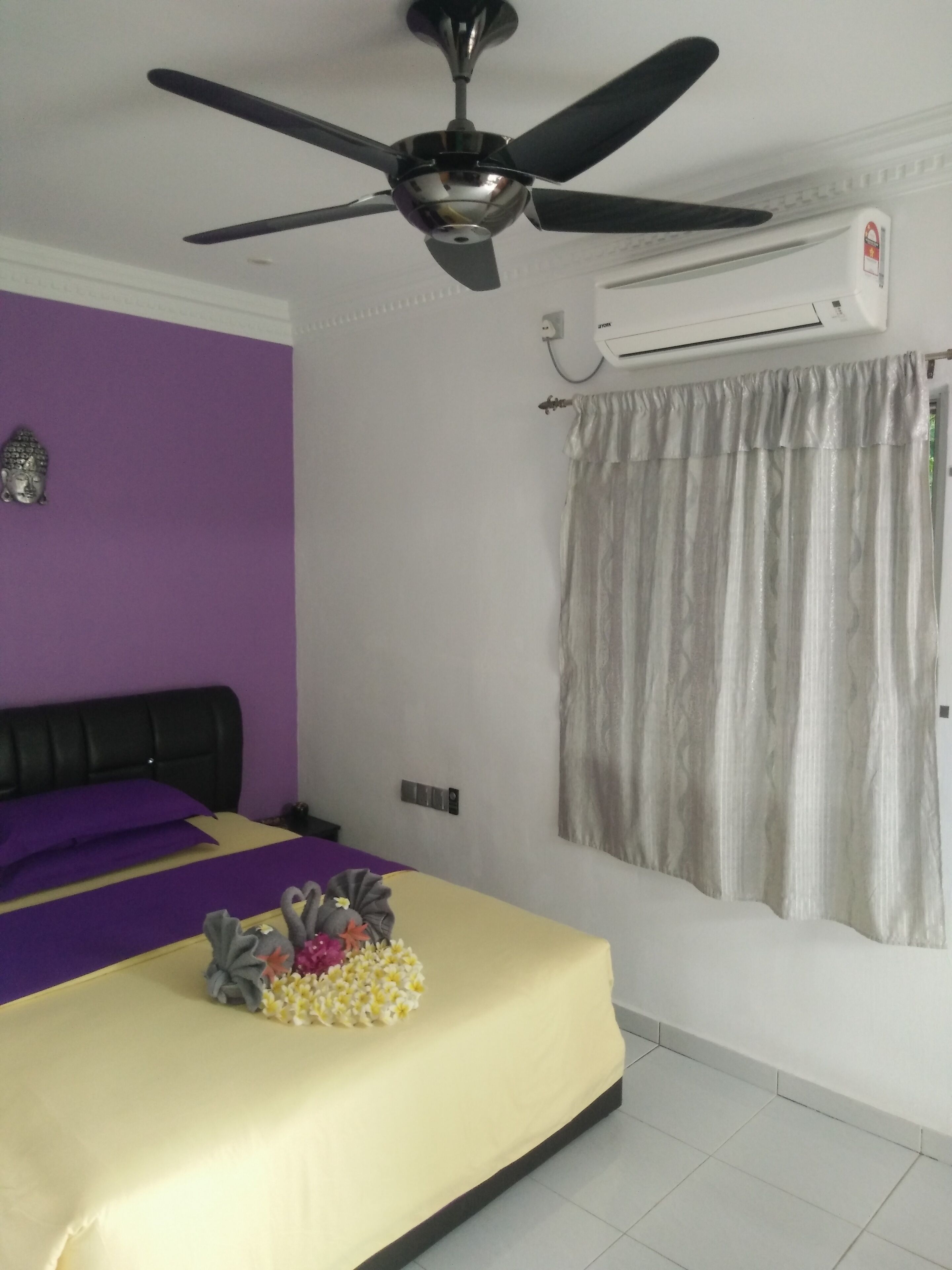 A bedroom with a bed, a ceiling fan, an air conditioning unit, and a window with curtains.