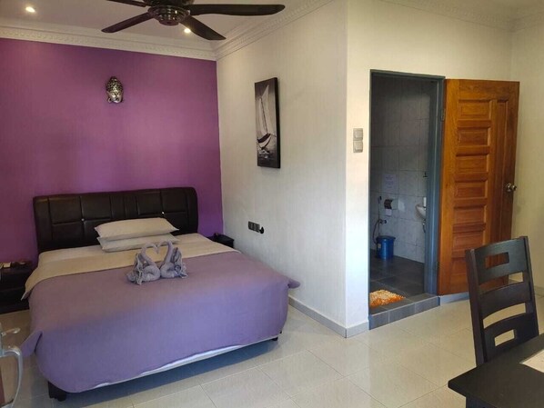 A bedroom with a bed, a ceiling fan, a door, and a small table.