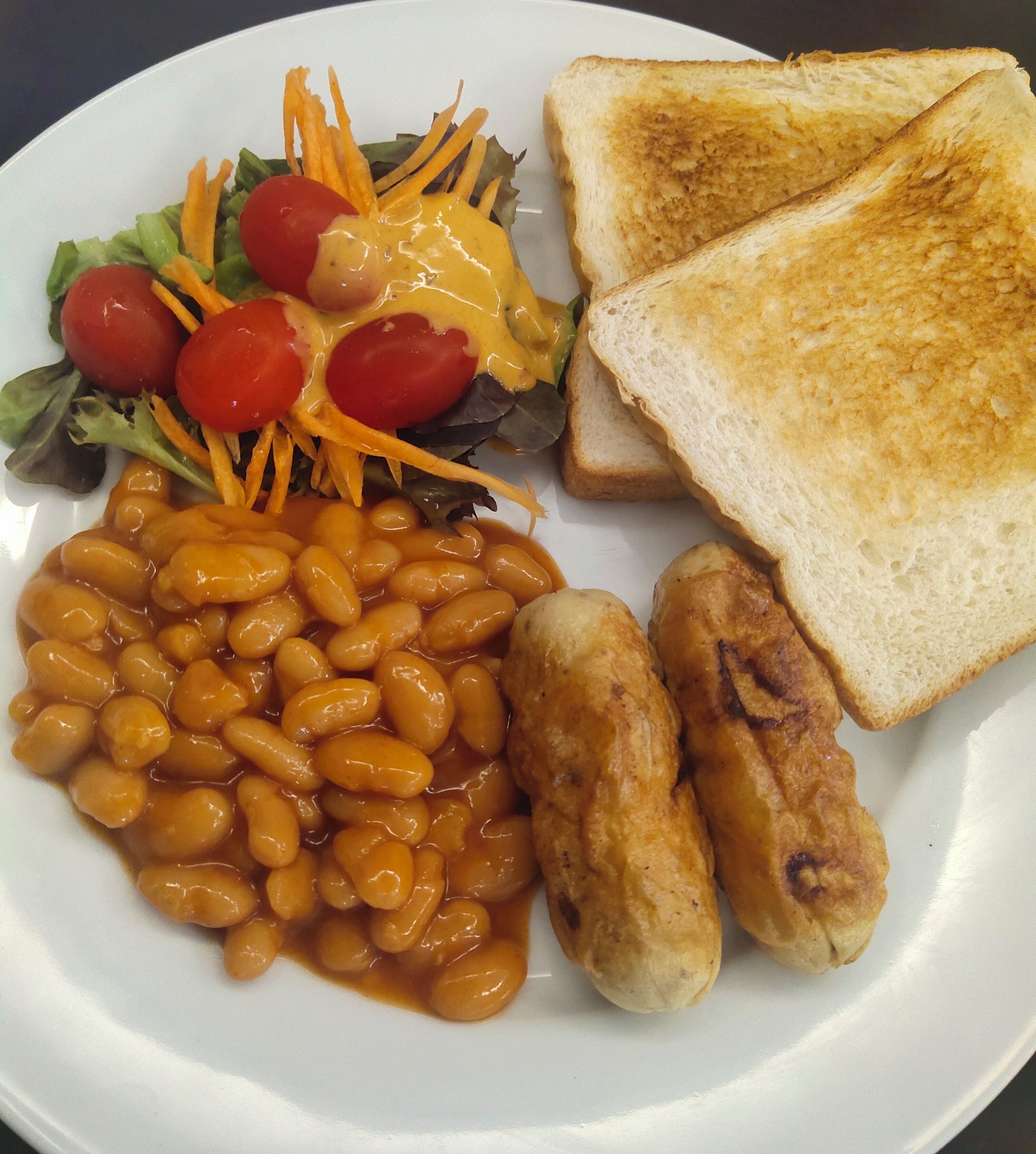 Un plato con frijoles, salchichas, tostadas y una ensalada.
