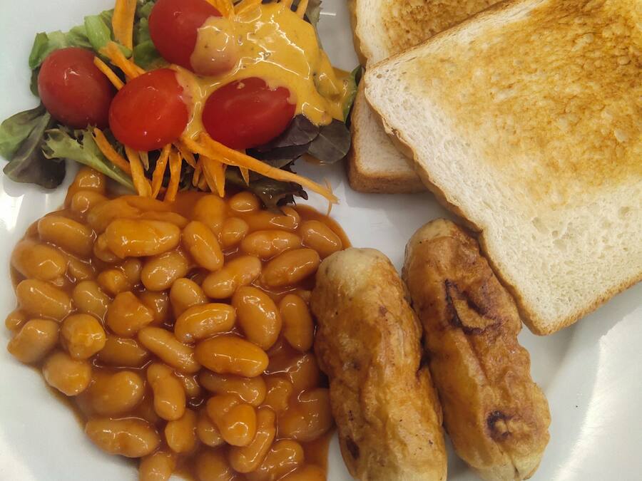 Un plato con frijoles, salchichas, tostadas y una ensalada.