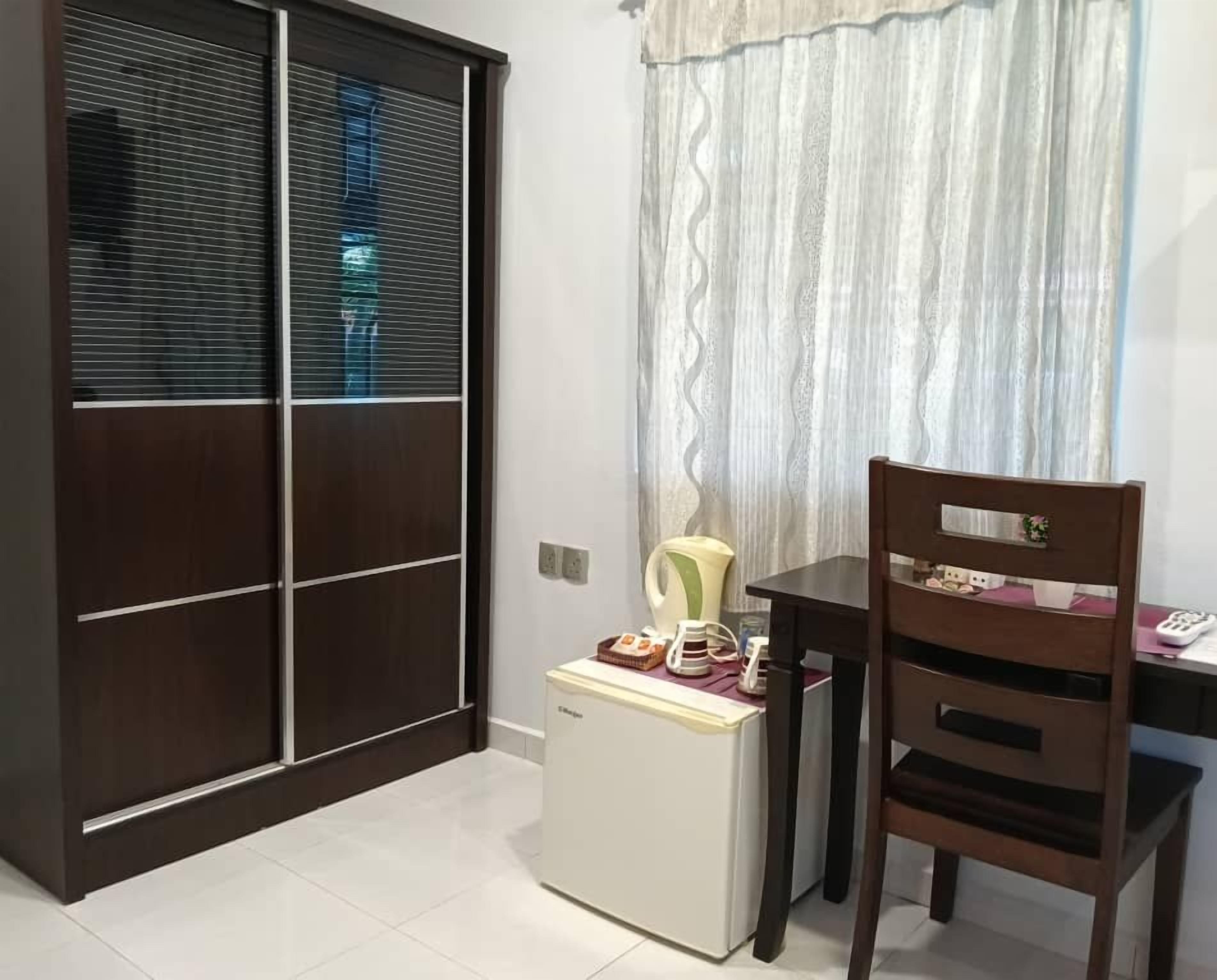 A compact room with a sliding door, a small refrigerator, a wooden chair, and a table with a kettle and cups.