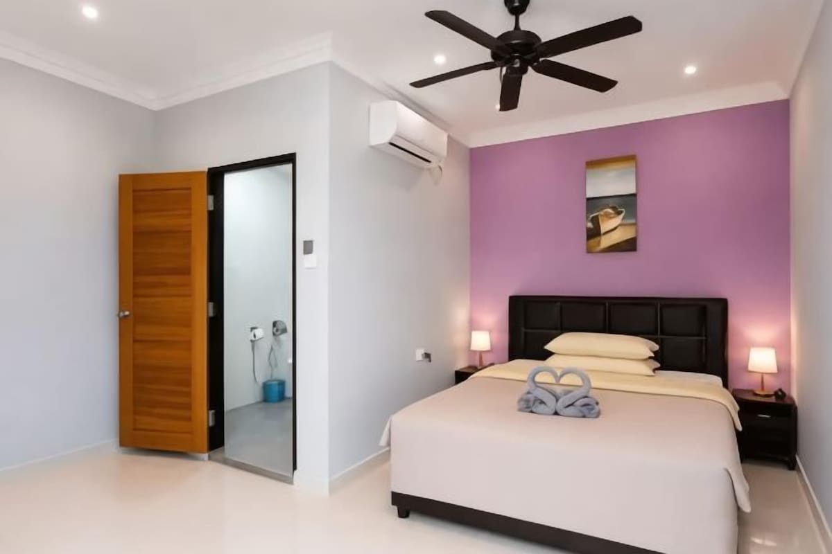 Une chambre à coucher comprenant un lit, un ventilateur de plafond, une table de chevet et un climatiseur fixé au mur.