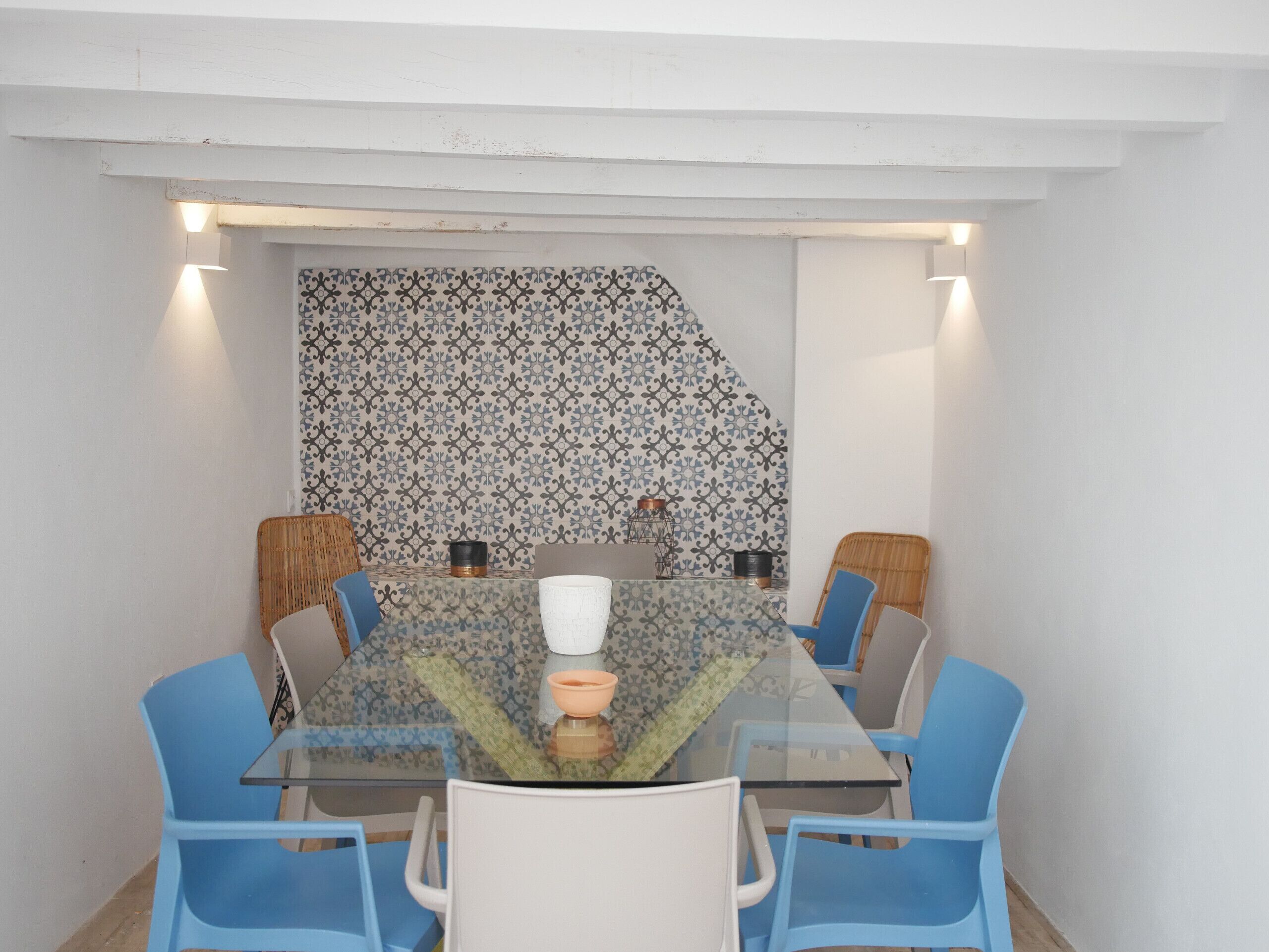A conference room with a glass table, blue chairs, and patterned wallpaper.
