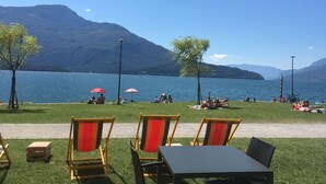 A lakeside seating area with chairs and tables, a clear view of the lake, and mountains in the background. - Cosy apartment for 4 guests with WIFI, TV and terrace (Domaso)