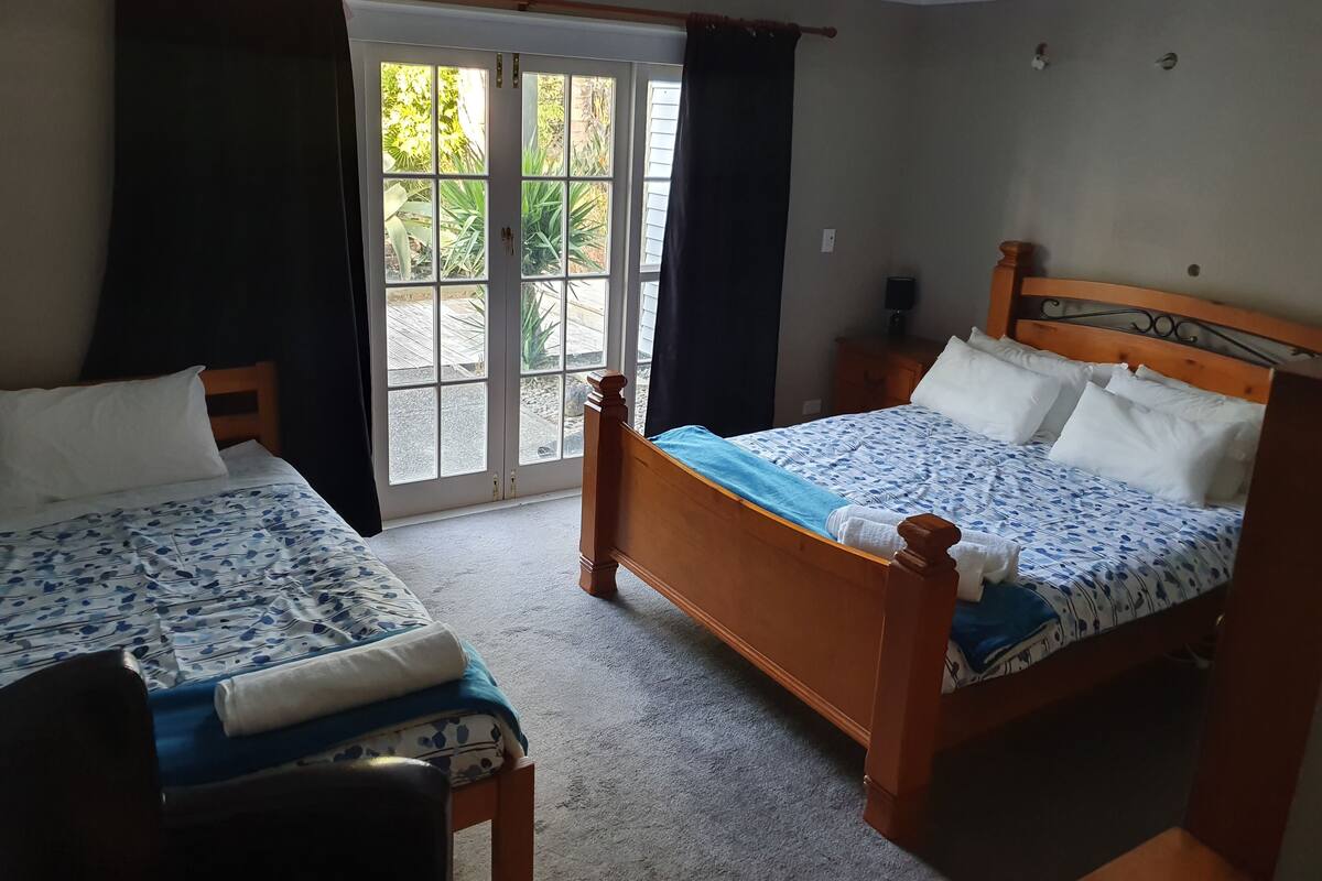 A hotel room with two beds, a large window, and a view of greenery outside.