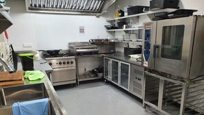 Une cuisine professionnelle équipée d’appareils électroménagers en acier inoxydable, notamment une cuisinière, un four et un réfrigérateur.