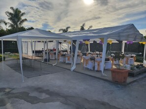 An outdoor event space with white tents, tables with white and orange chairs, and balloons.