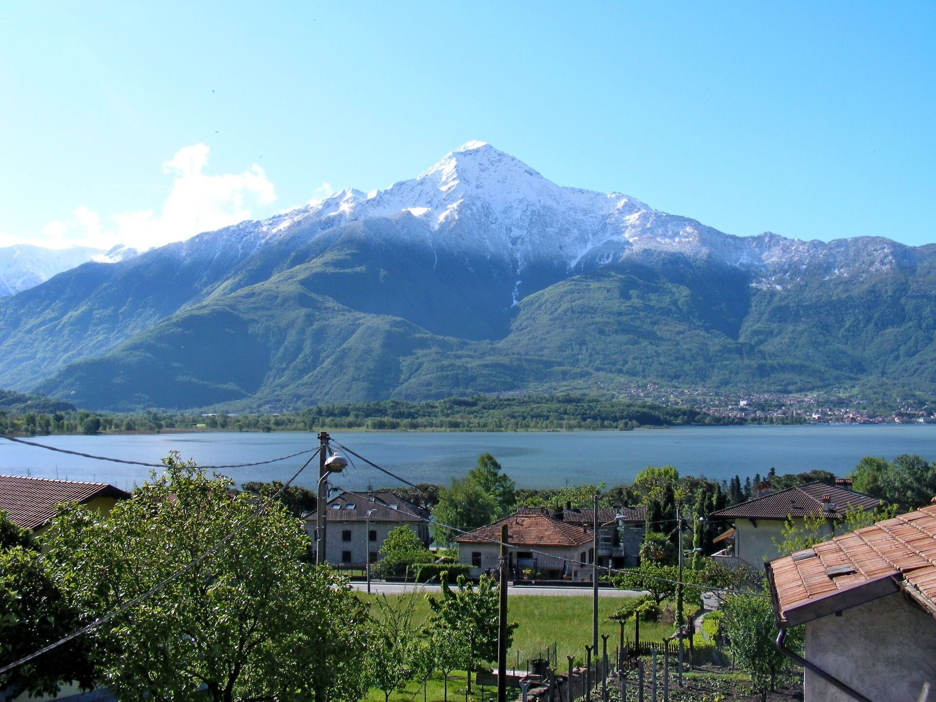 A mountain with a snow-capped peak, a lake, and a residential area with houses and greenery in the foreground.