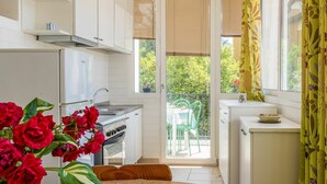 A kitchen with a stove, sink, and cabinets. There is a window with blinds, a door leading to a balcony, and a table with a vase of flowers. - Nice apartment for 5 people with WIFI, TV, balcony and pets allowed (Gera Lario)