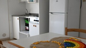 A kitchen with a white refrigerator, a stove, and a sink. There are two placemats on the table. - M150 - Marcelli, two-room apartment directly on the beach (Marcelli)