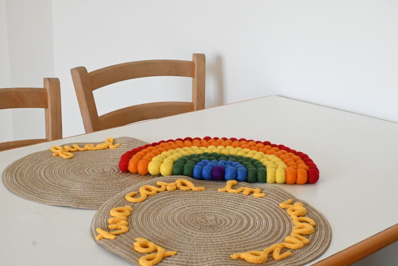 A table with two woven placemats featuring text and a rainbow design.