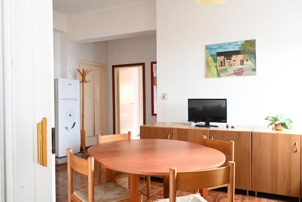 A dining area with a wooden table and chairs, a television on a wooden cabinet, and a painting on the wall.