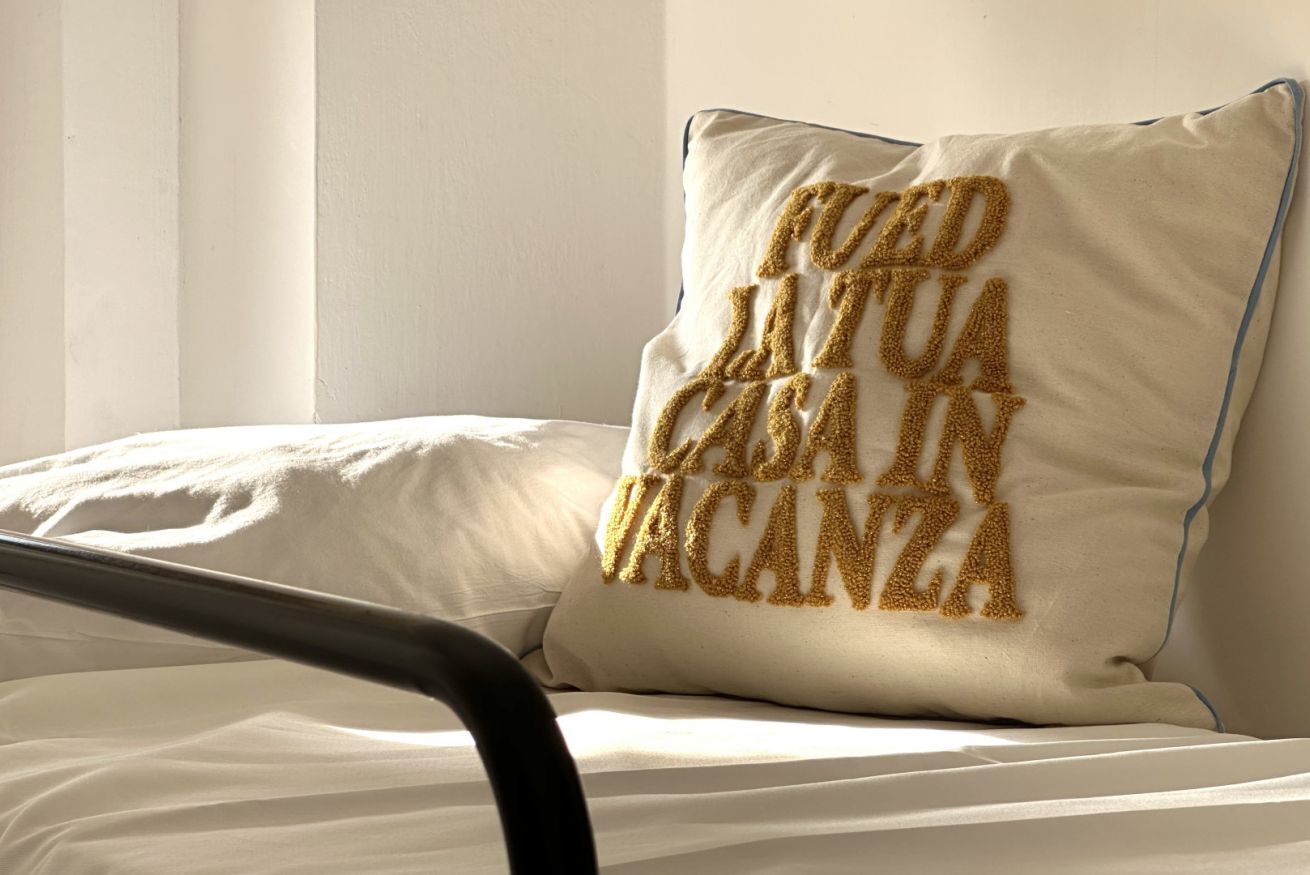 Una cama con un almohadón que lleva bordado un texto.