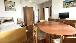 Ein Zimmer mit einem Bett, einem Esstisch, Stühlen, einem Fernseher und einem Kühlschrank.