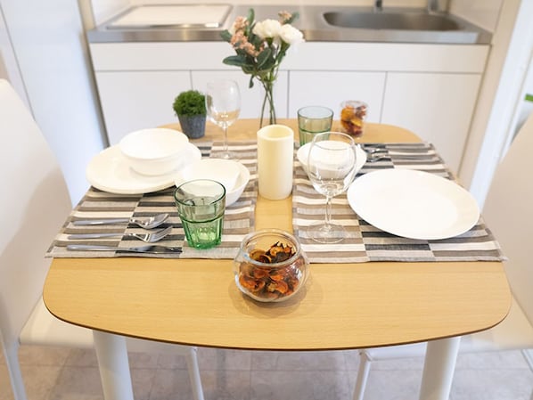 A dining table set with plates, glasses, cutlery, and a candle, with a kitchen in the background.