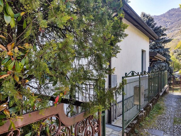 A narrow cobblestone path leading to a building with a white facade and a green metal fence. - Beautiful apartment for 4 guests with WIFI, TV, terrace and pets allowed (Gera Lario)