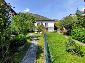 A white building with a balcony, surrounded by lush greenery and a stone pathway. - Beautiful apartment for 4 guests with WIFI, TV, terrace and pets allowed (Gera Lario)