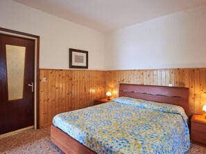 A bedroom with a wooden headboard, a bed with a floral bedspread, a bedside lamp, and a framed picture on the wall. - Beautiful apartment for 4 guests with WIFI, TV, terrace and pets allowed (Gera Lario)