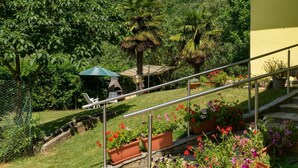 Ein Garten mit einer Steintreppe, Sitzgelegenheiten im Freien und Blick auf einen üppigen Wald.