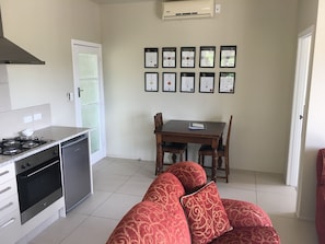 A compact kitchen with a gas stove, oven, and dishwasher, a dining table with chairs, and a sofa in the living area.