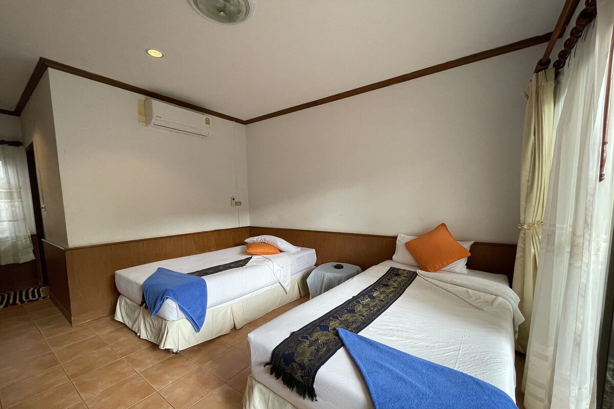 Una habitación de hotel con dos camas individuales, una mesita redonda y un ventilador de techo.