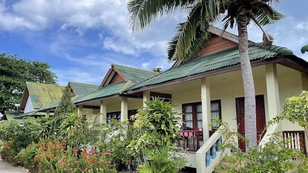 A row of traditional-style buildings with green roofs and a well-maintained garden with various plants and flowers. - Sea Breeze Bungalow (Koh Samui)