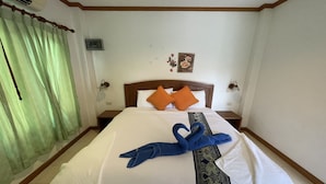 A hotel room with a neatly made bed, green curtains, a wooden headboard, and a small wall decoration. - Sea Breeze Bungalow (Koh Samui)