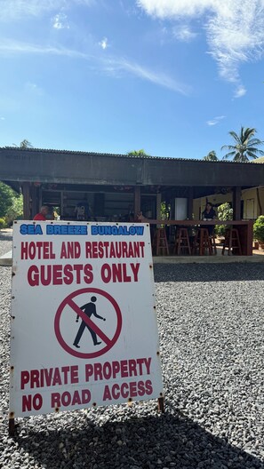 Señal que indica 'SOLO HUÉSPEDES DEL HOTEL Y RESTAURANTE SEA BREEZE BUNGALOW, PROPIEDAD PRIVADA, SIN ACCESO POR CARRETERA', con vista del exterior del edificio y cielo despejado.