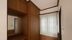 A room with wooden wardrobes, a mirror, a window with a sheer curtain, and a tiled floor. - Sea Breeze Bungalow (Koh Samui)