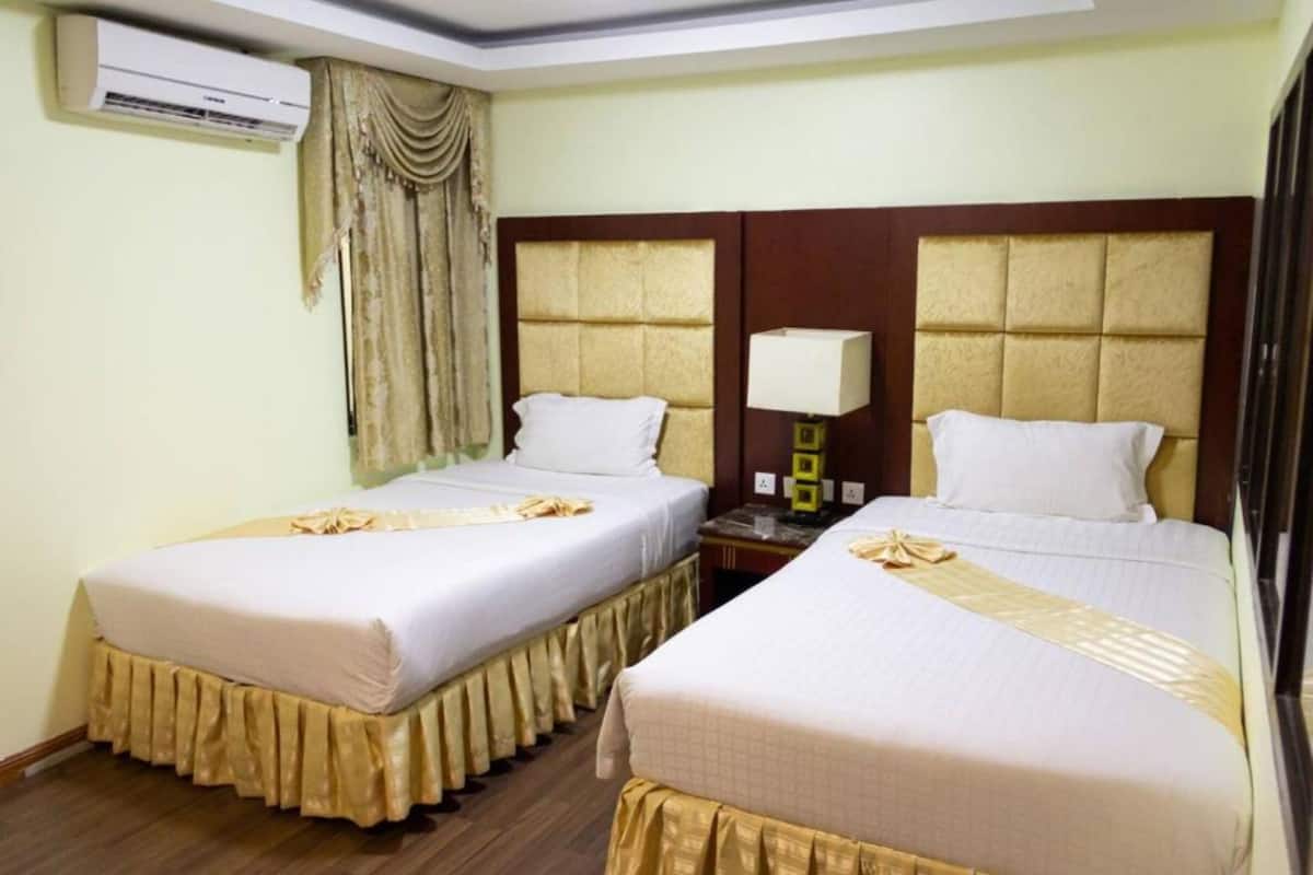 Quarto de hotel com duas camas, uma mesa de cabeceira, um abajur, ar condicionado e cortina.