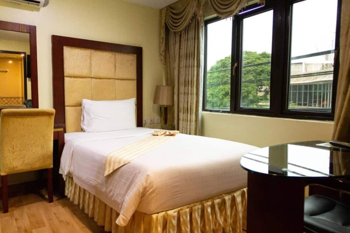 Quarto de hotel com cama, uma cadeira, escrivaninha e janela com vista.