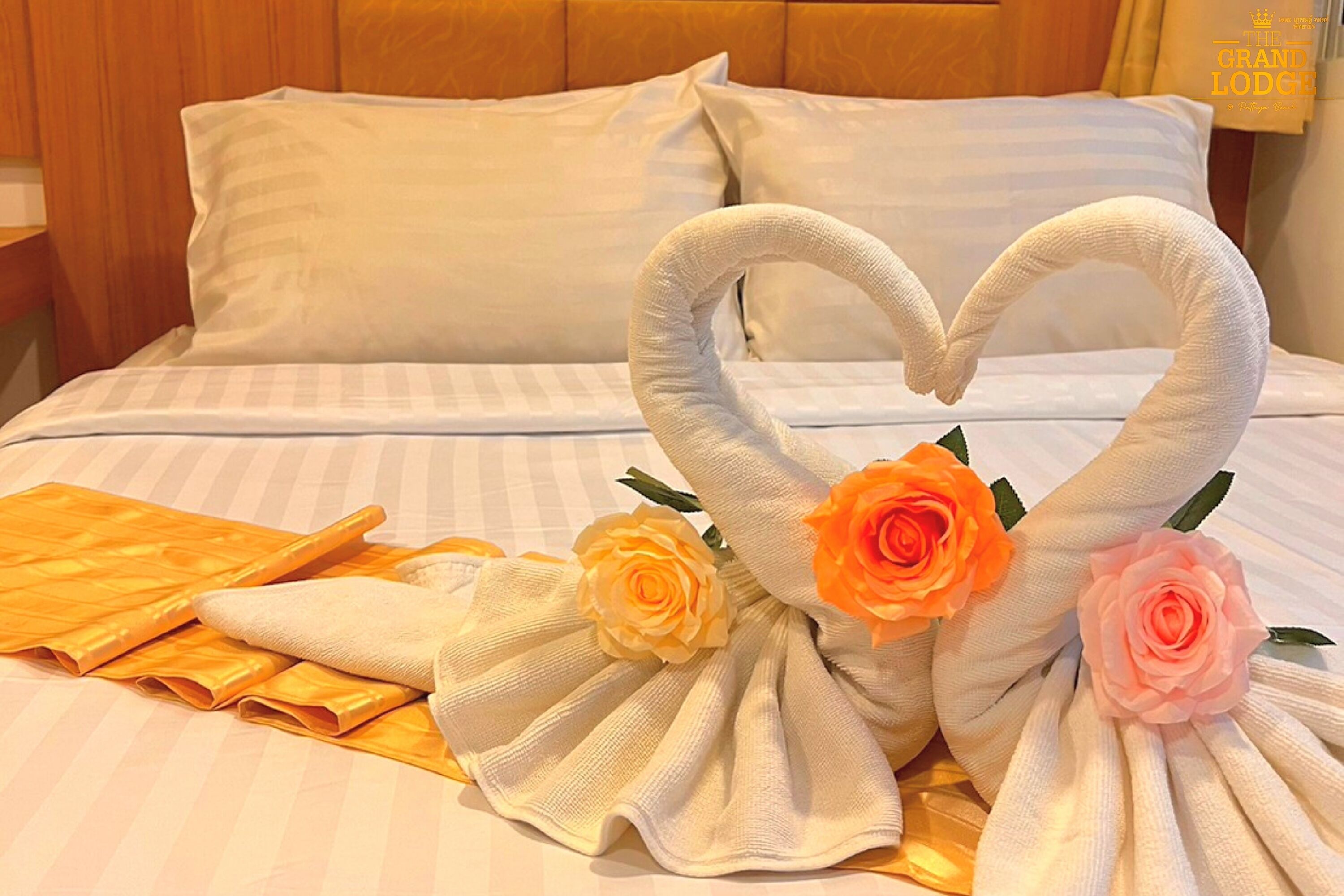 A bed with a heart-shaped towel arrangement and roses.