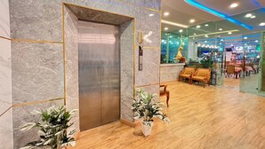 Un hall d’hôtel moderne avec un mur en marbre, un ascenseur, un comptoir d’accueil et un espace salon doté de meubles en bois.