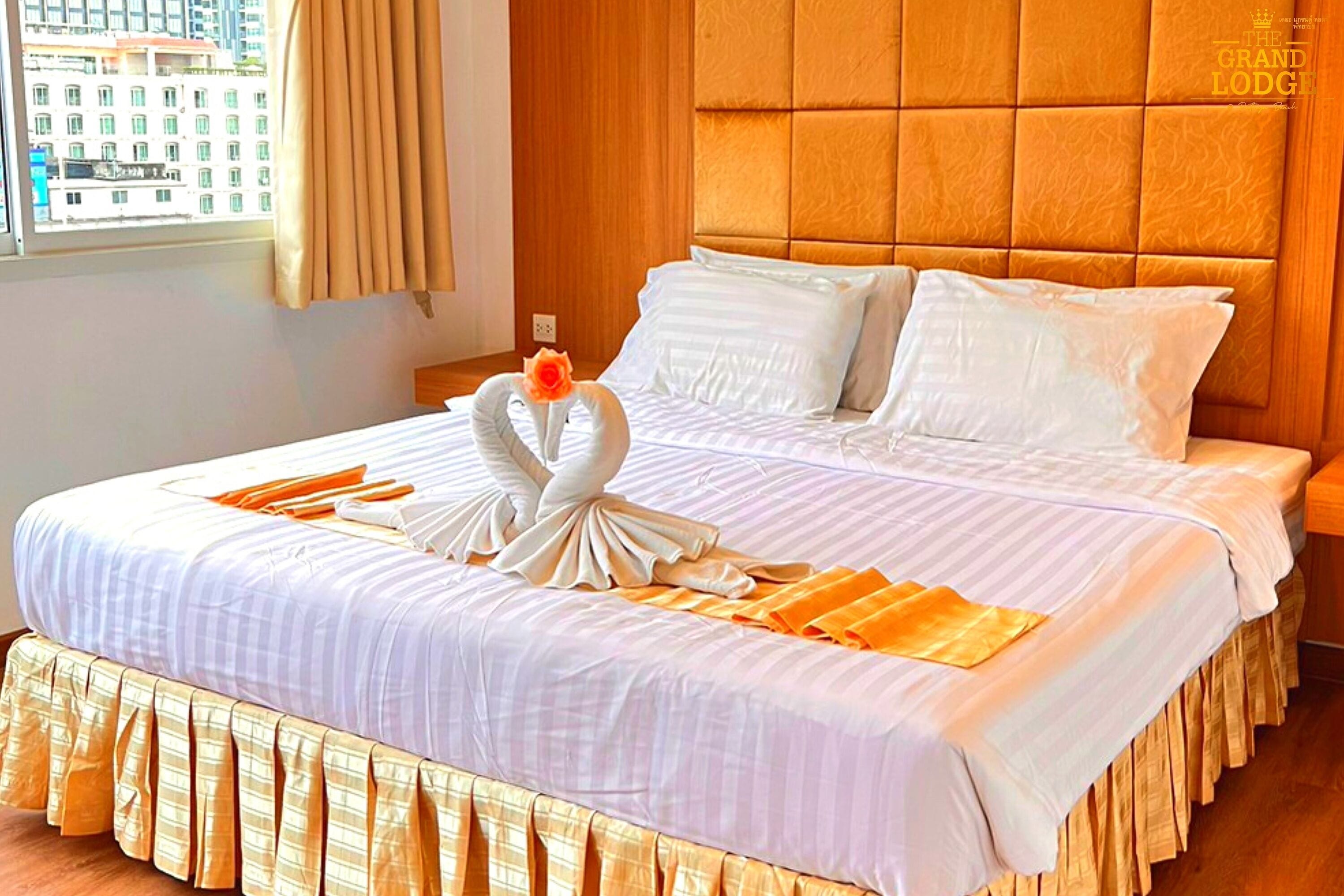 A neatly made bed with a swan-shaped pillow arrangement, a window with curtains, and a wooden headboard.