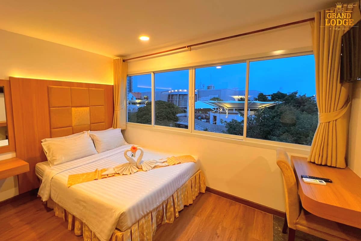 Quarto de hotel com uma cama grande, uma escrivaninha e janela com vista para a cidade.
