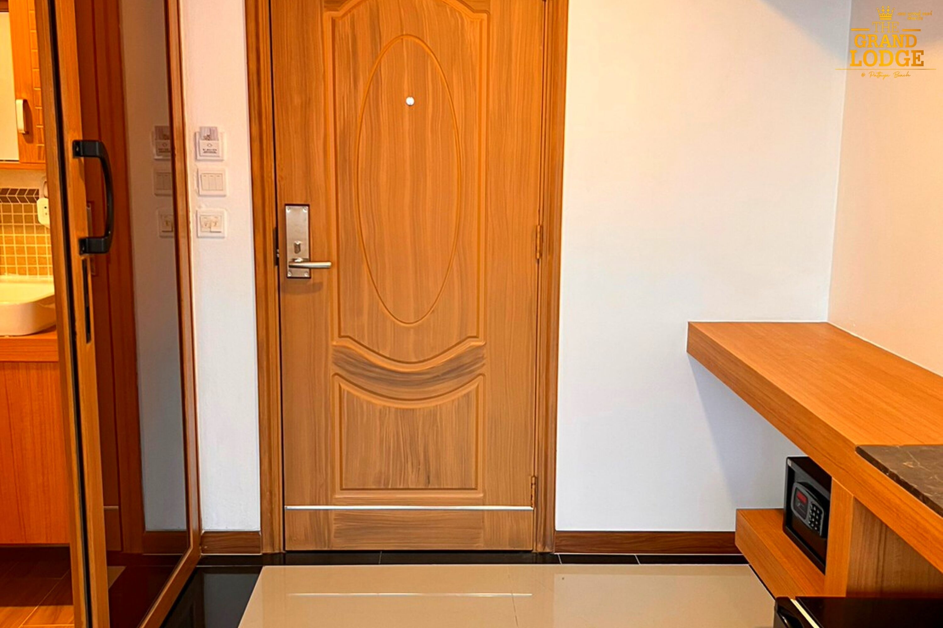 Una porta in legno con una maniglia, un piccolo dispositivo elettronico su uno scaffale e un pavimento piastrellato.